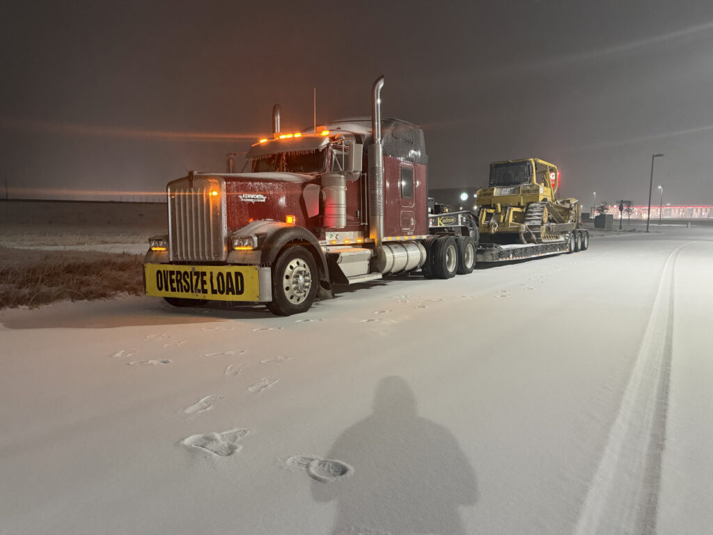 Oversize load truck hauling bulldozer in snowy weather